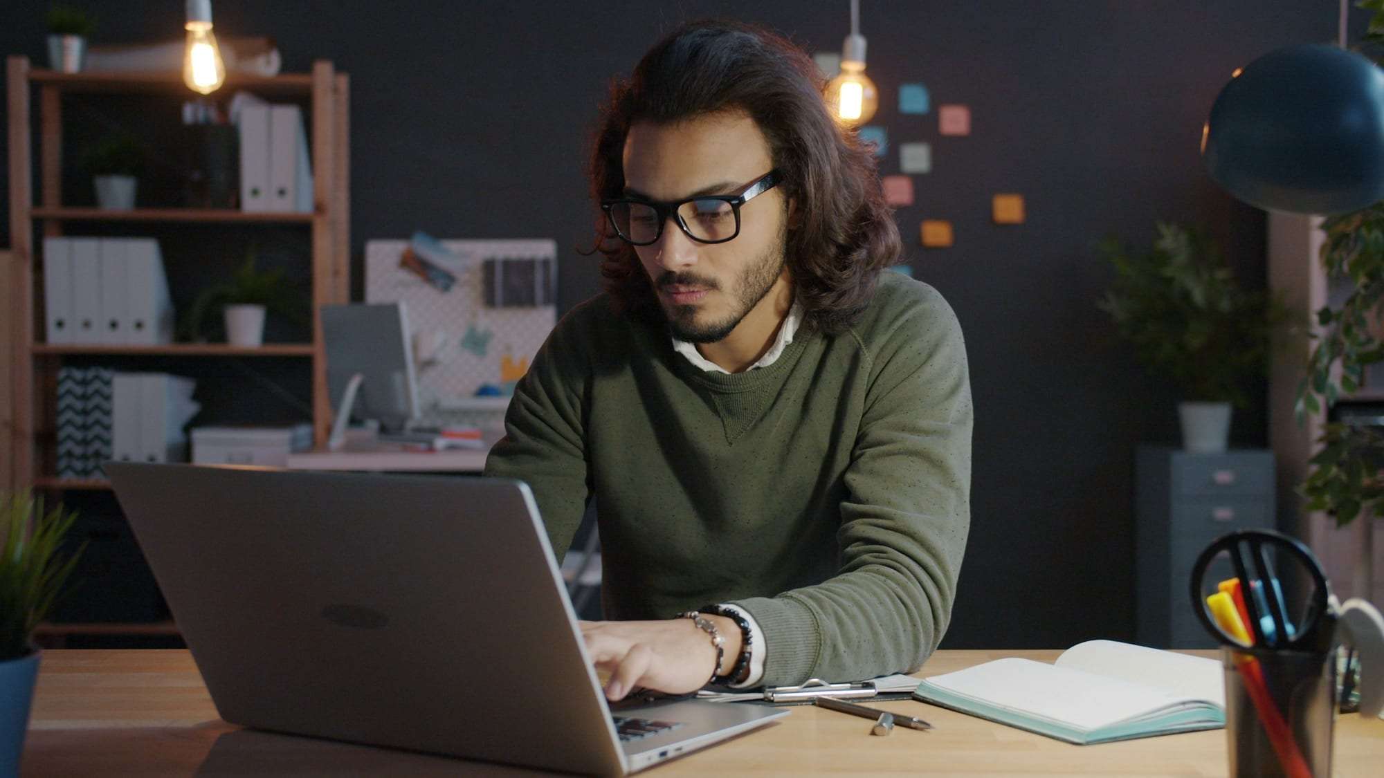 A young man in glasses studying at a laptop at home in the evening